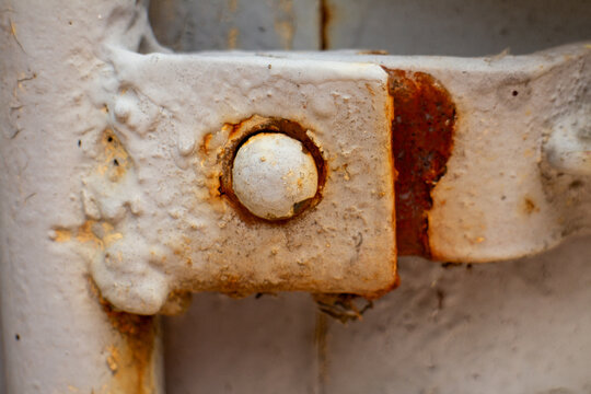 Close-up of a rusted metal hinge with old white paint on an industrial door