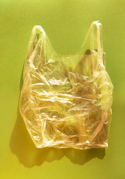 Transparent plastic shopping bag with crumpled texture displayed against a solid green background, highlighting its lightweight and flexible design for retail use