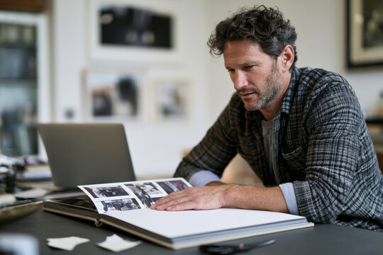 A man thoughtfully examines an old photo album filled with black-and-white photographs, appreciating the historical context and personal stories behind each image.
