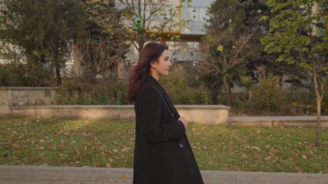 Young woman in black coat walking through city park in autumn