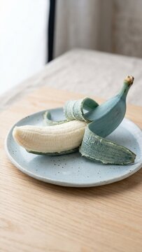 Peeled Blue Java banana resting on a ceramic plate on wooden table in soft light