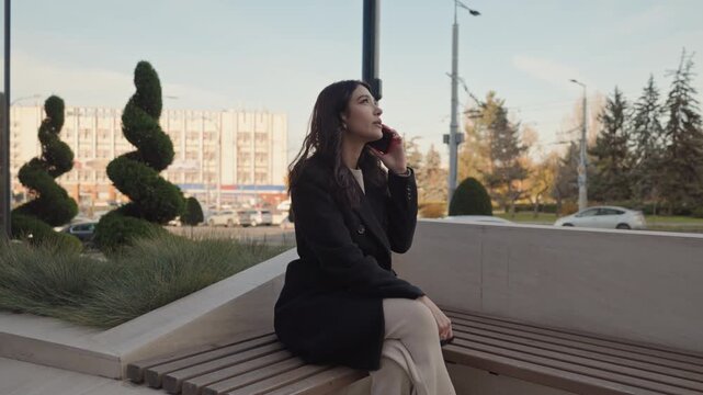 Young businesswoman making phone call on city park bench
