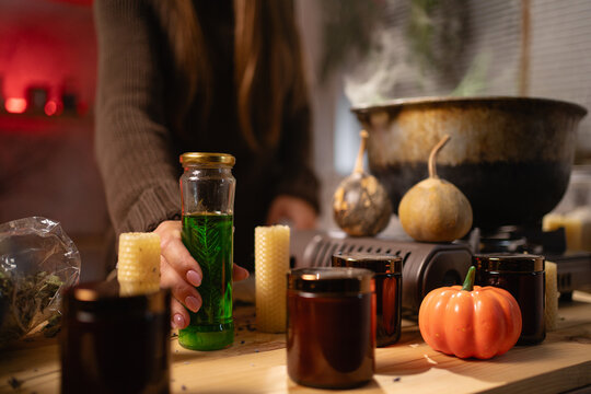 A realistic witch brewing a potion in a cauldron. Close-up of a hand picking up a jar of liquid. Everyday life intertwined with traditional witchcraft, magic, and a mystical atmosphere