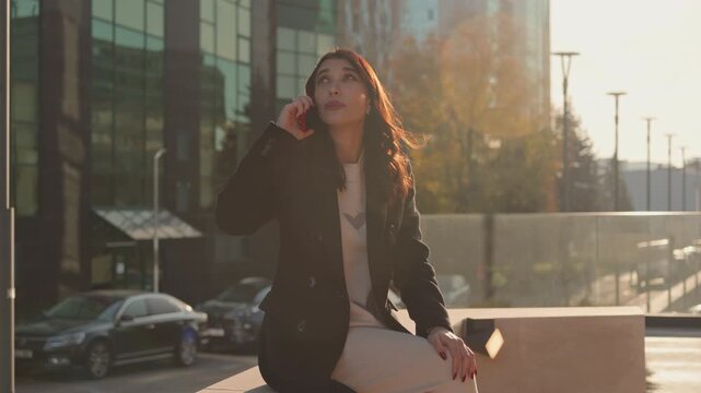 Cheerful young woman making smartphone call outdoors at golden hour