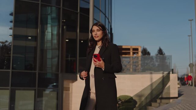 Professional woman holding phone in sunny urban business district