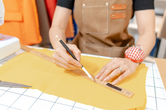 Professional fashion designer working in a modern sewing studio, measuring, marking and cutting fabric patterns for custom clothing production. Creative apparel development