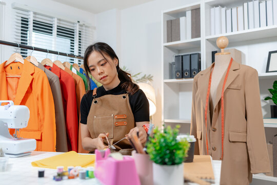 Professional fashion designer working in a modern sewing studio, measuring, marking and cutting fabric patterns for custom clothing production. Creative apparel development