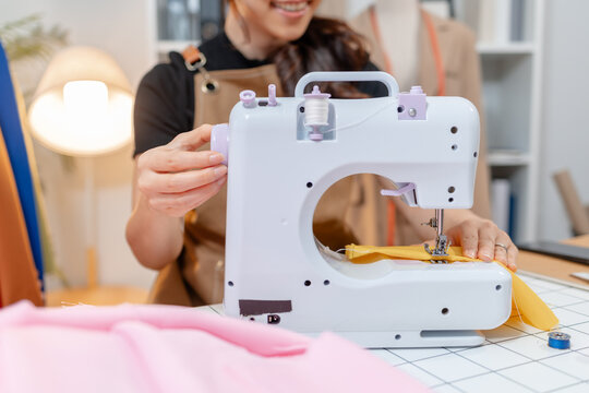 Professional fashion designer using a sewing machine in a modern studio while managing creative apparel production. Handmade craftsmanship, tailoring and small business workflow.