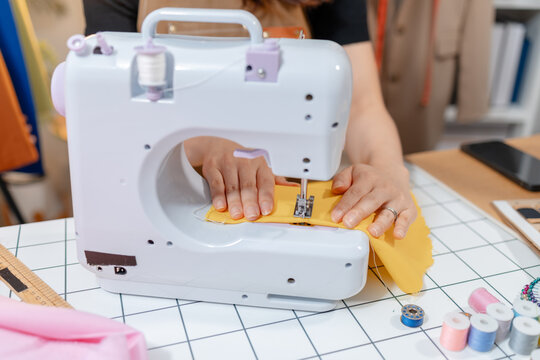 Professional fashion designer using a sewing machine in a modern studio while managing creative apparel production. Handmade craftsmanship, tailoring and small business workflow.