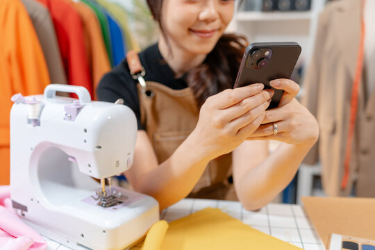 Professional fashion designer using a sewing machine in a modern studio while managing creative apparel production. Handmade craftsmanship, tailoring and small business workflow.