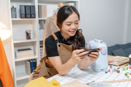 Professional fashion designer using a smartphone while managing a sewing studio and organizing tailoring supplies. Creative apparel production, small business and handmade craftsmanship.