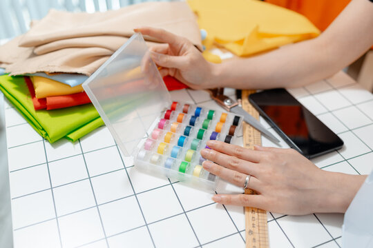 Professional fashion designer using a smartphone while managing a sewing studio and organizing tailoring supplies. Creative apparel production, small business and handmade craftsmanship.