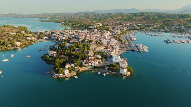 Drone shot of a sleek black superyacht and workboat resting on the calm Aegean Sea near Porto Heli, Greece, with pine-lined shores framing the tranquil bay.