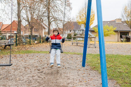 Young boy having fun swinging in playground outdoors
