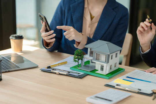 Real estate agent and client discussing house investment plan with laptop and house model on desk.