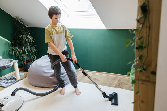 Boy vacuuming rug at home completing domestic chores