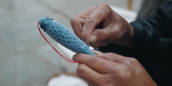 Elderly hands holding a traditional blue fabric sachet with red string