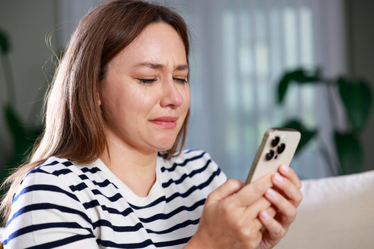 Heartbroken woman crying while looking at smartphone