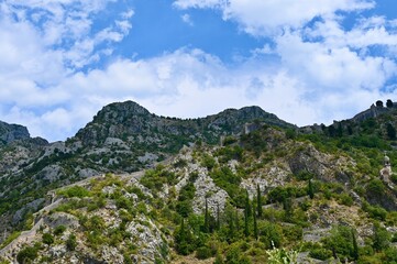 Fototapeta premium A scenic horizontal view of medieval stone fortifications stretching along steep mountain ridges, with a church belfry visible in the lower foreground under a partly cloudy blue sky.