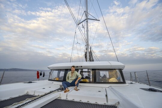 Young man sitting on the deck of a sailing catamaran, sailing trip, Rhodes, Dodecanese
