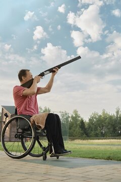 Outdoor portrait of a senior man using a wheelchair, holding a rifle up to the sky waiting for flying target
