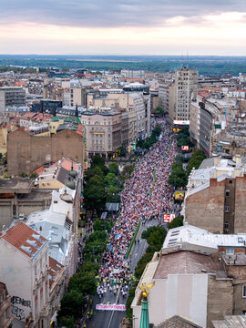 Belgrade, Serbia - 14 September 2026: Aerial view of students and citizens marching through city streets to deliver election signatures, surrounded by historic buildings under a soft sky.