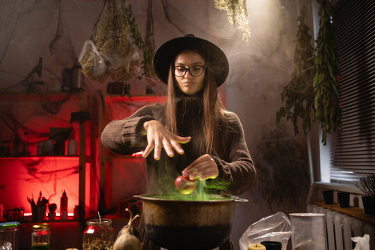 She holds a red apple, waves her hand, and recites a spell. A realistic witch brewing a potion in a cauldron. Everyday life intertwined with traditional witchcraft, magic, and a mystical atmosphere