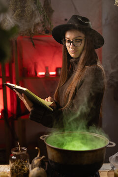 A woman is holding a book of spells and looking into a cauldron. A realistic depiction of a witch brewing a potion in a cauldron. Everyday life intertwined with traditional witchcraft,