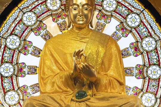 In the main chedi of Wat Phra That Sorn Kaew, the gilded Buddha statue shines out against a luminous glass mandala that fills the space with light and colour. The delicate patterns of the window and the gentle radiance of the robe combine to create an atmosphere of quiet contemplation. This photograph captures the unique harmony of spiritual symbolism, exquisite craftsmanship and meditative tranquillity: the main chedi (Phra That), Wat Phra That Sorn Kaew, Khao Kho Mountains, Phetchabun Province, Isan, Thailand