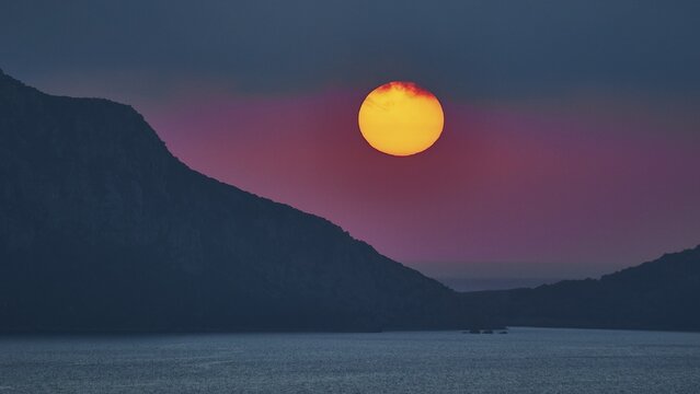 Sun sets over water between dark mountains, Navarino Bay, Pylos, Peloponnese, Greece