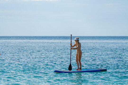 Paddleboarding, woman, ocean. Woman enjoys stand up paddleboarding on calm blue ocean with clear sky.