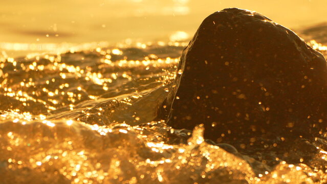 Sunset ocean rock golden waves splash against a dark rock on the beach during a warm summer evening with copy space