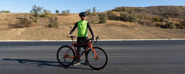 Cyclist riding bicycle on road against clear sky. A man in an outfit stands with a bicycle on an autumn sunny day. © Budjak Studio