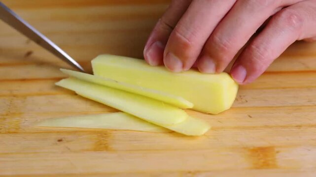 Hand slicing red bell pepper and ginger on wooden cutting board for cooking preparation
