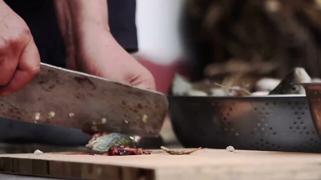 Chef slicing fresh fish with cleaver on wooden cutting board in kitchen prep station