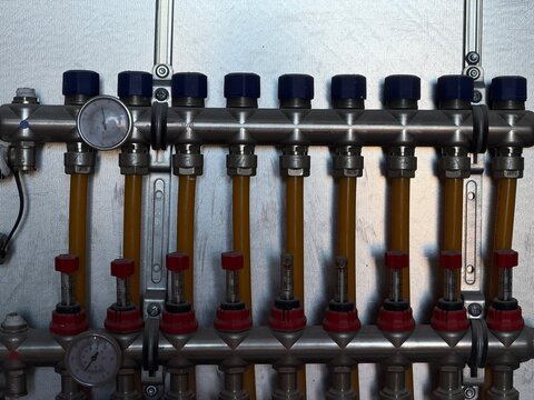 Stainless steel heating manifold distributing warm water through multiple pipes, regulating flow for an efficient underfloor heating system installation, modern home comfort