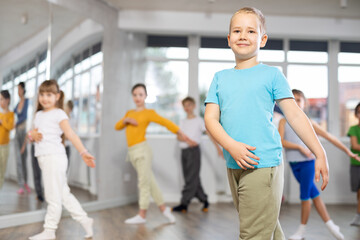 Obraz premium During dance workshop, boy with team of young like-minded children learn to dance modern dances, doing movement with unrecognizable teacher. Studio school for amateur and professional dancers