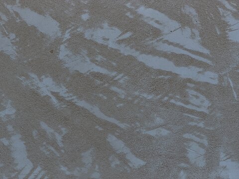 Rough grey brown plaster wall with uneven, distressed texture and weathered patches, creating an abstract grunge backdrop ideal for architectural, urban or design projects