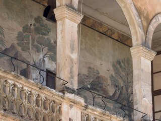 Old architectural facade in manacor. Balearic islands. Spain. Featuring an aged fresco mural depicting a serene natural landscape with trees. Mountains. And birds © Tetyana
