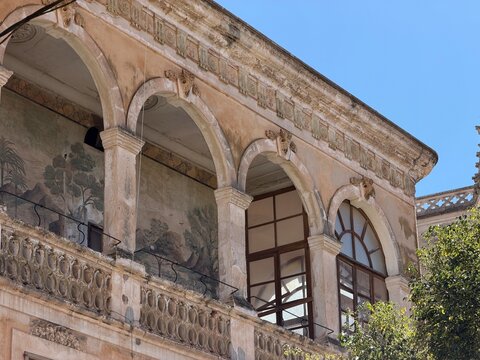 Historic building facade in manacor featuring ornate architectural details. Weathered arches. Balustrade. And ancient landscape murals