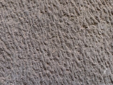Rough stone wall texture with diagonal chiseled grooves, creating a weathered and rustic background pattern, showcasing ancient masonry and natural rock surface detail