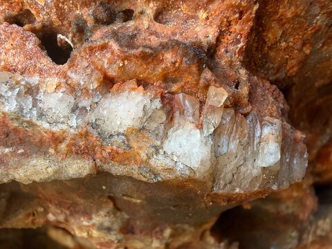 Quartz crystals forming in reddish rock, showing geological stratification and natural mineral deposits in cova des correu, manacor, balearic islands, spain
