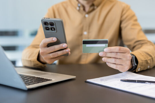 Online payment and e commerce security, person using smartphone and credit card for digital banking transaction at office desk. Secure mobile app usage for financial management and shopping.