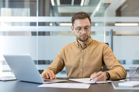 Productivity and focus in the workplace, professional man working on laptop and writing notes at office desk. Business strategy and task management.