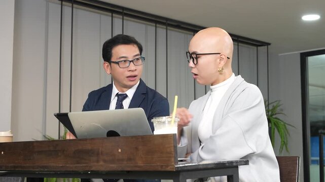 A smart-looking Korean female employee wearing glasses sits with an Asian male colleague in a coffee shop, working on her laptop, reading emails, and attending a meeting.
