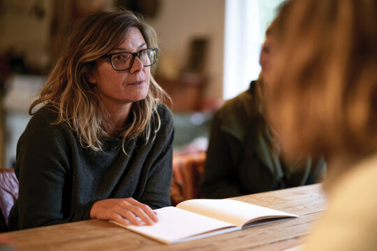 A woman engages in a thoughtful discussion during a meeting, reflecting deep concentration and a sharing of ideas with her peers in a cozy workspace environment.