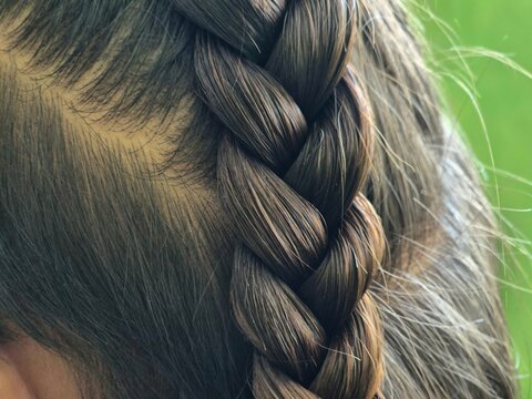 Close-up of neat French braid hairstyle on brunette hair with blurred green background