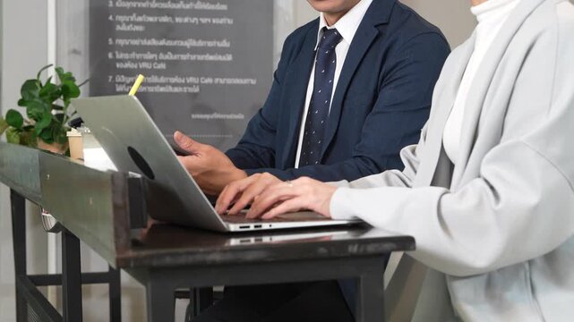 Hands of male and female employees typing on laptop keyboards in a coffee shop or coworking space.