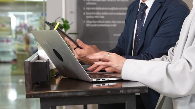 Hands of male and female employees typing on laptop keyboards in a coffee shop or coworking space.