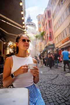 Young woman drinking coffee at outdoor cafe near Galata Tower in Istanbul, Turkey. Tourist enjoying local cafe culture and relaxed summer travel lifestyle